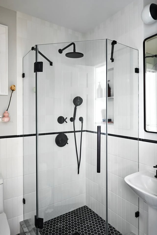 A bathroom featuring a white vertical rectangular wall tiles accented by a thin black border and paired with black hexagonal floor tiles. 