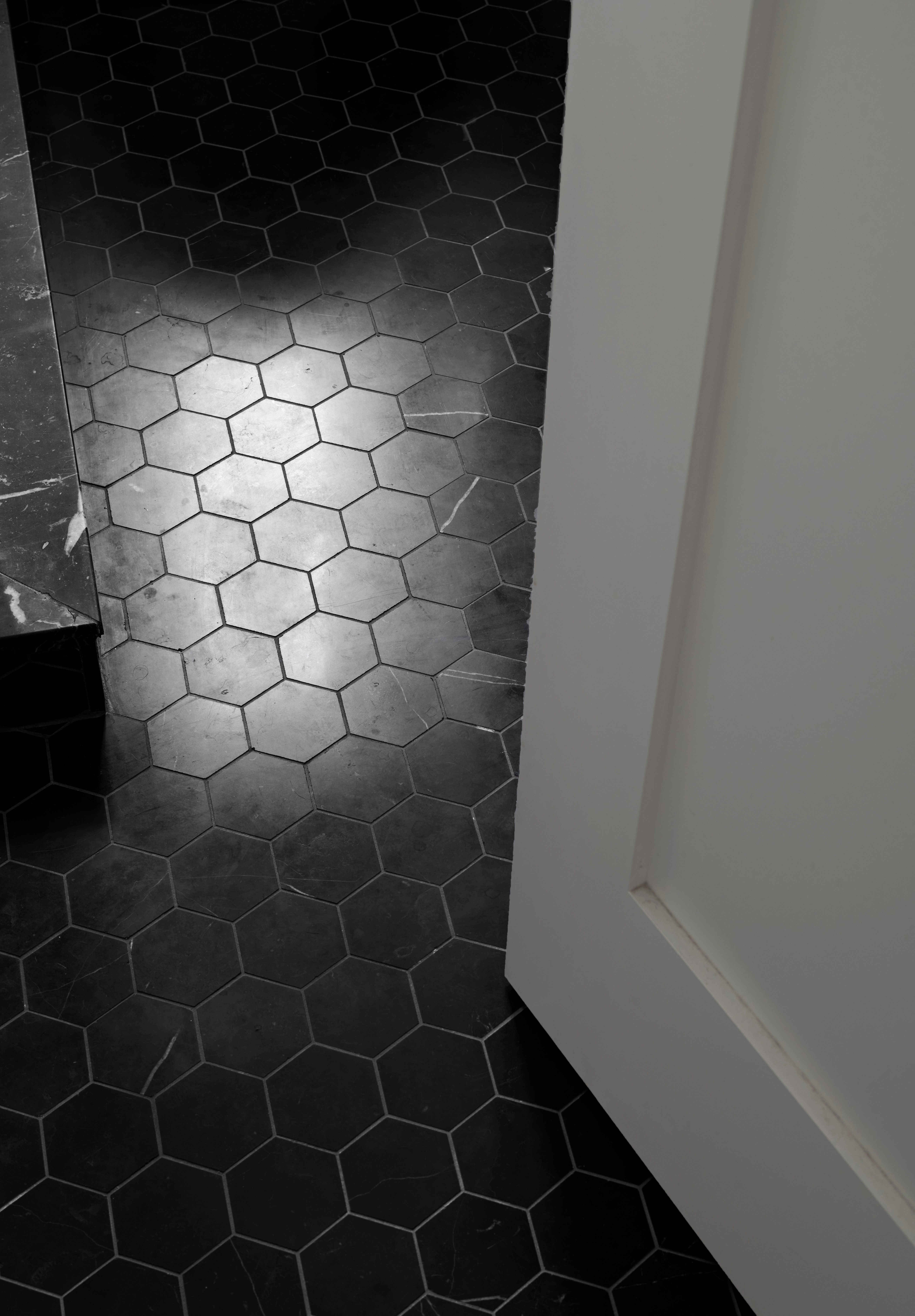 Black hexagon floor tiles next to an open white door.
