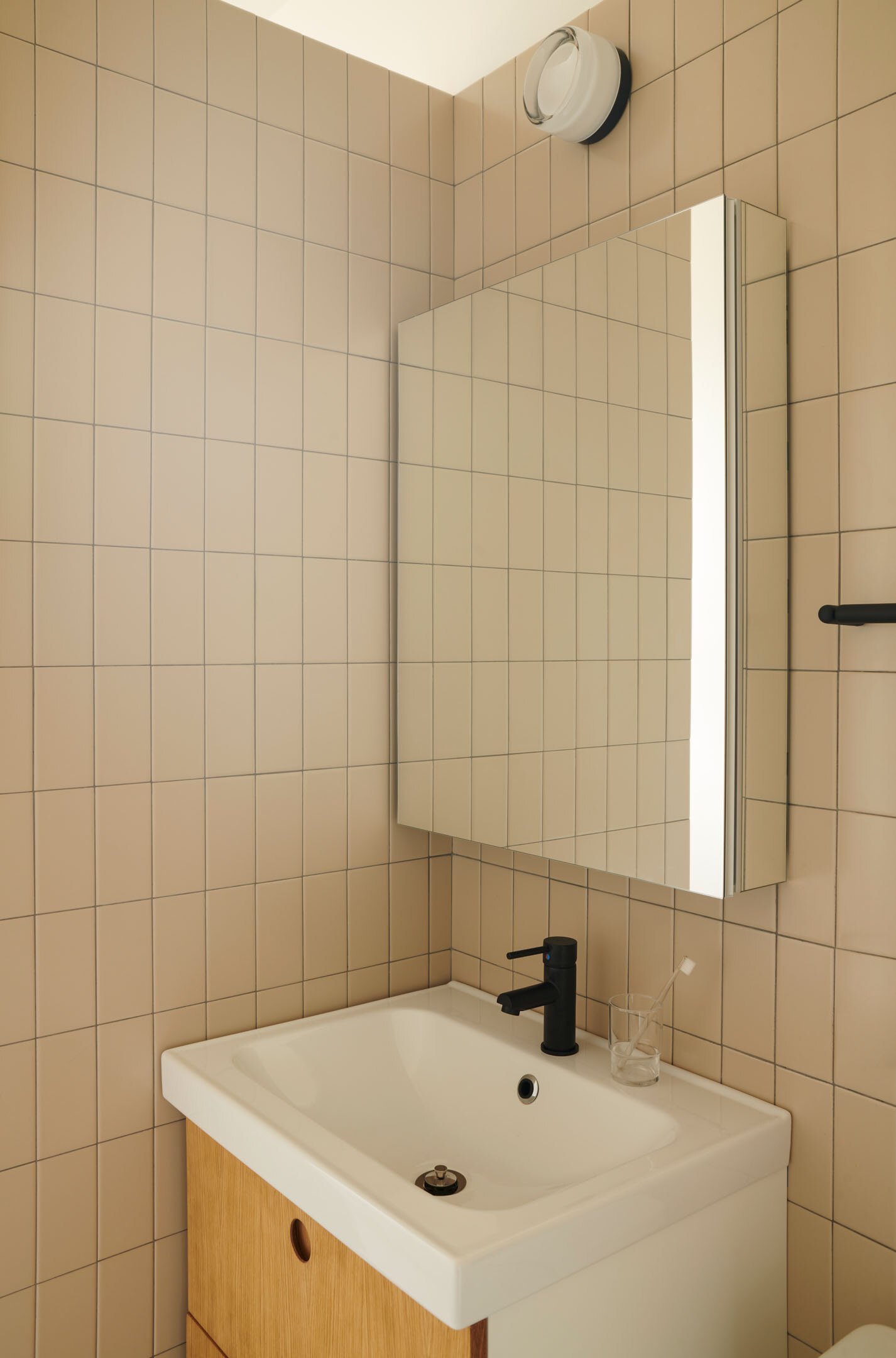 Beige tiled bathroom with a wood vanity and mirror.