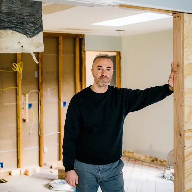 A man in a black sweatshirt stands in a doorway during a home renovation.