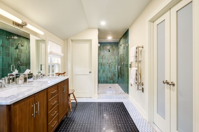 A modern bathroom featuring a wood vanity with a marble countertop, black and white floor tiles, and a walk-in shower with green tiling.