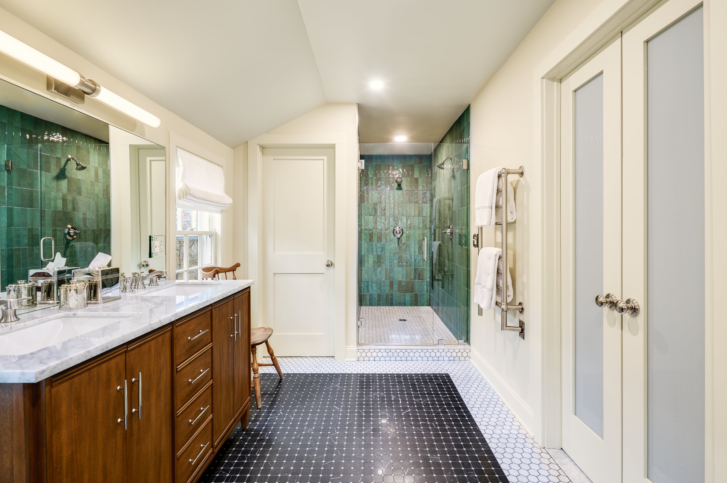 Green tiled shower, wooden vanity, and elegant marble floor.