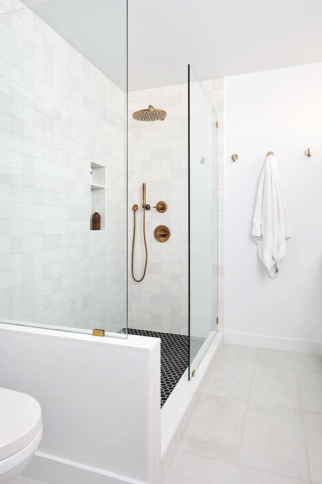 White bathroom with glass-enclosed shower and bronze fixtures.