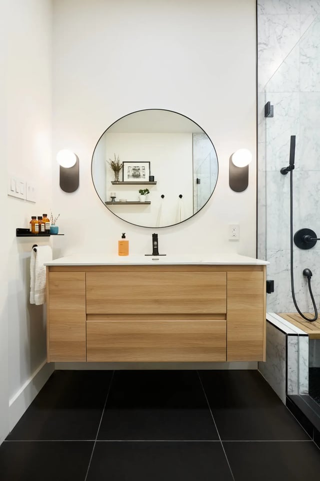 White bathroom with wood floating sink and black tiles.