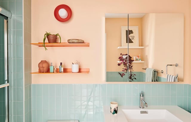 Bathroom with peach walls, light blue subway tiles, a large mirror, two orange floating shelves, a white sink, and a red circular light fixture.