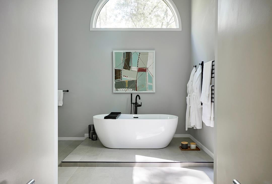 Modern bathroom with a white tub, arched window, and art.