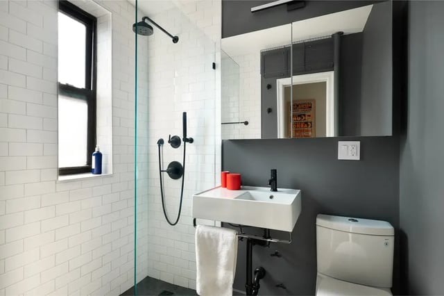 A modern bathroom featuring white subway tile, a glass shower enclosure with matte black fixtures, a white square sink, a toilet, and a medicine cabinet with mirrored doors.