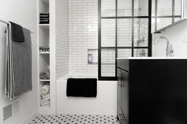 A modern bathroom with a black vanity, white subway tile bathtub, and a black-framed glass shower door.