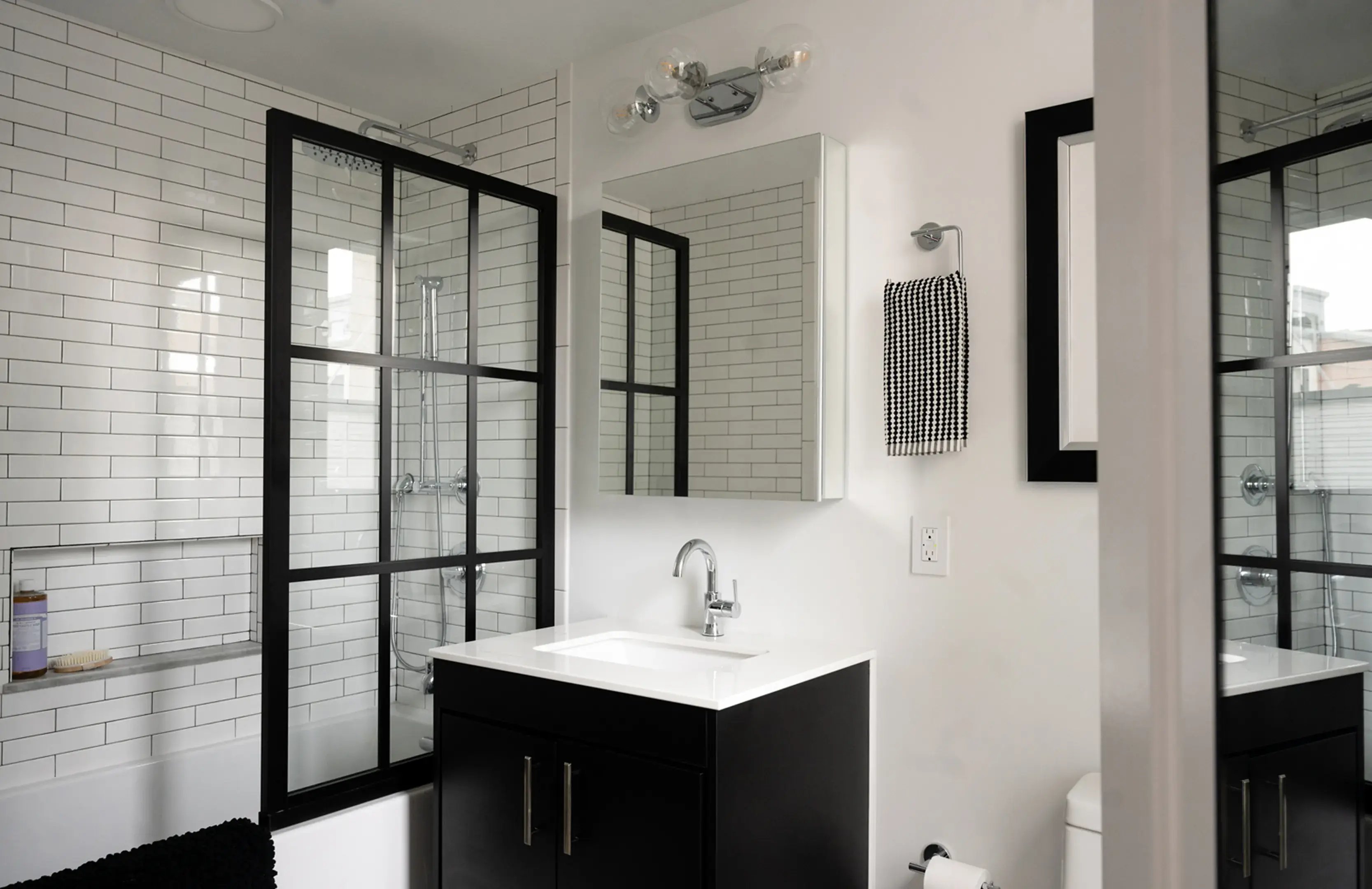 A modern black and white bathroom featuring a dark vanity, white subway tile, and a black-framed glass shower partition.