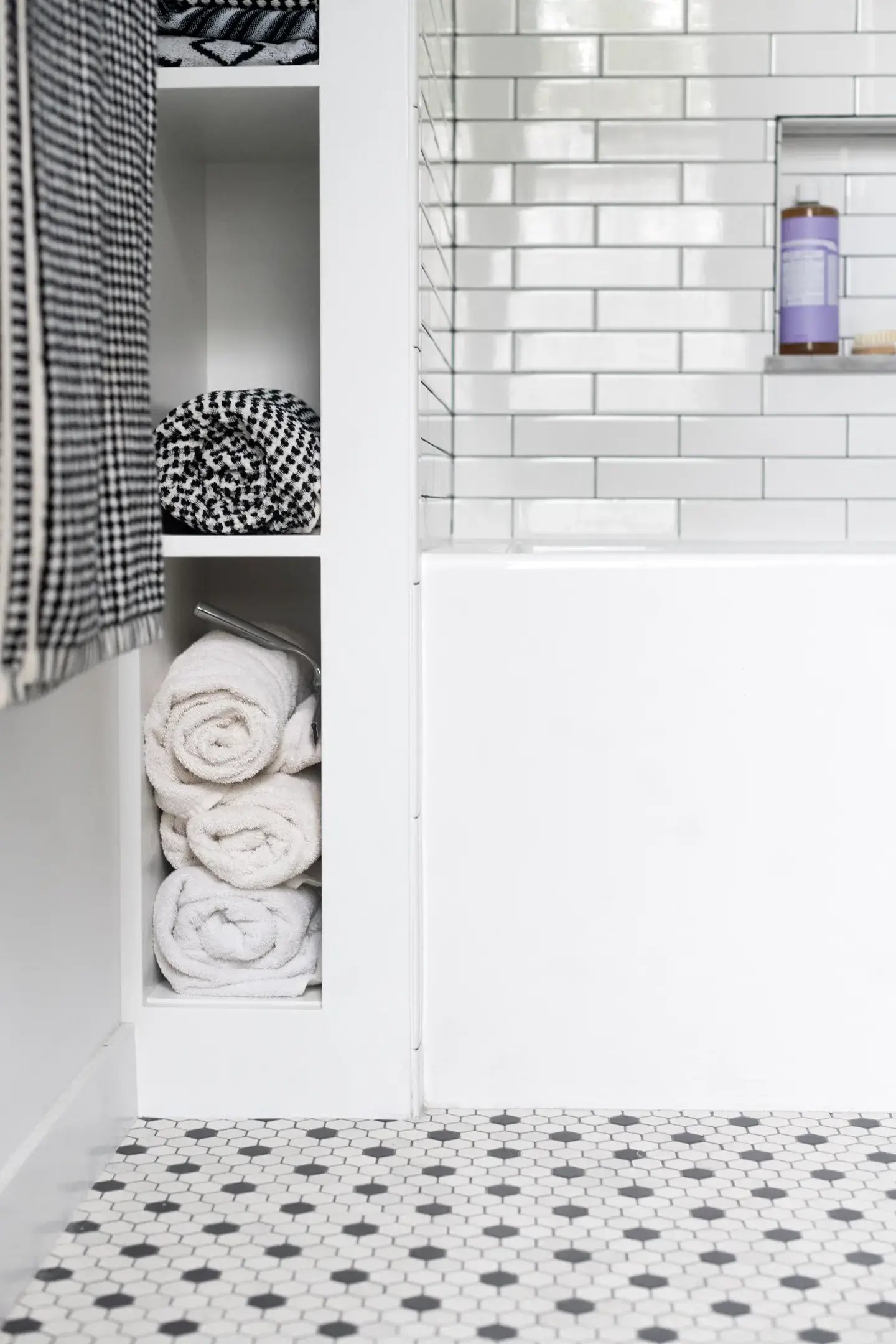A modern bathroom featuring a white bathtub, subway tile walls, and a built-in shelving unit filled with rolled towels.