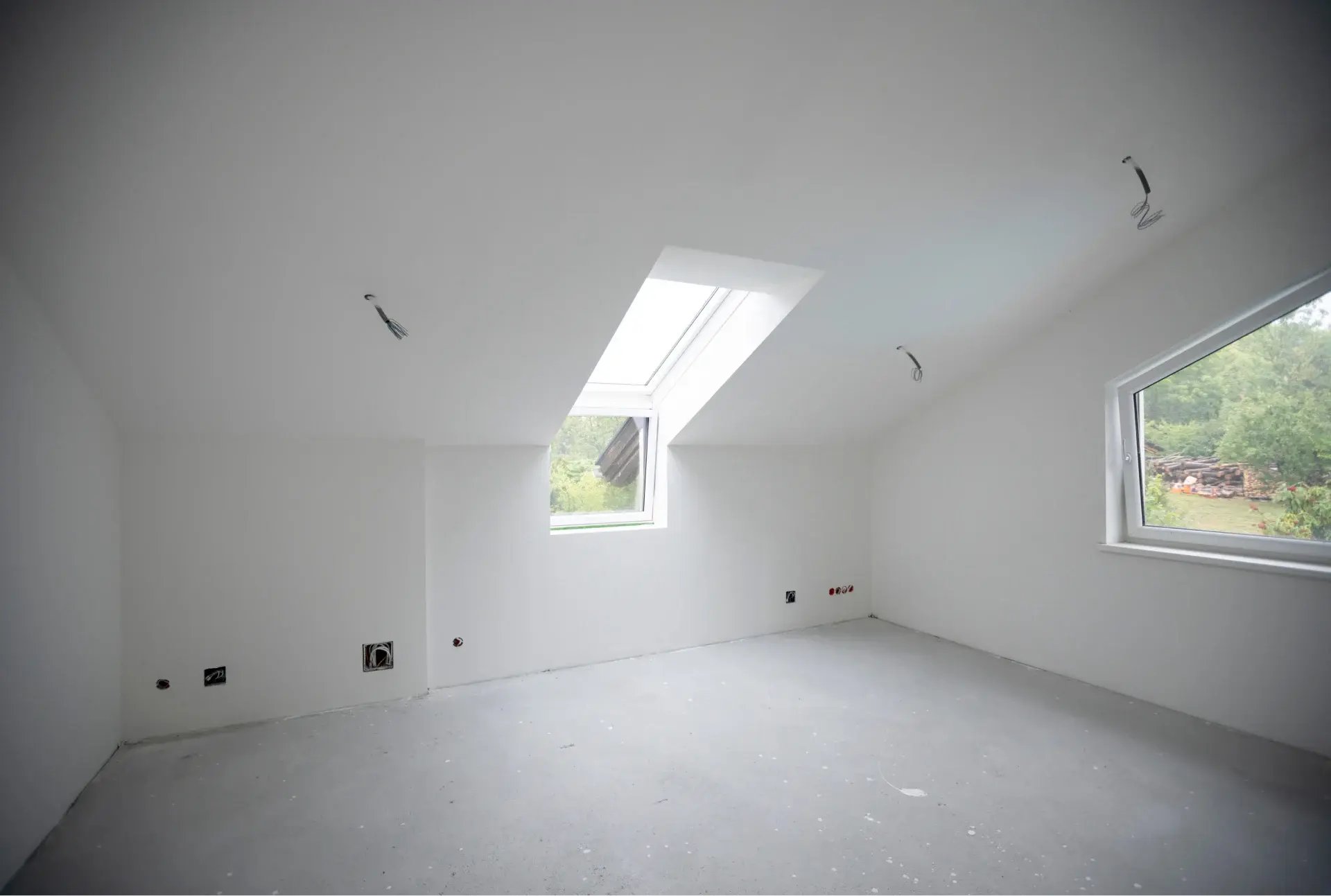 Empty white attic room with slanted ceiling and skylight.
