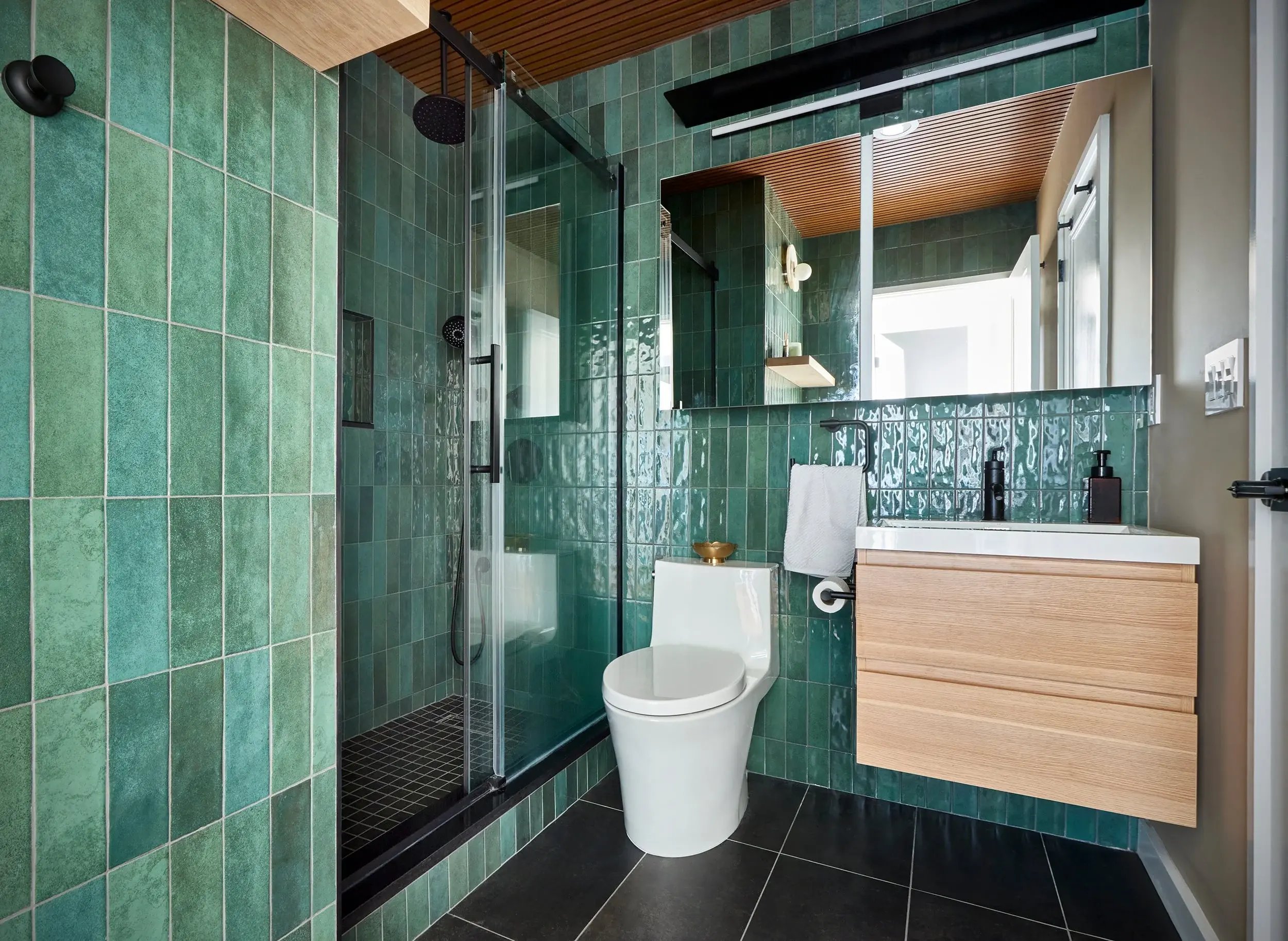 Modern bathroom with green tiles and a light wood vanity.