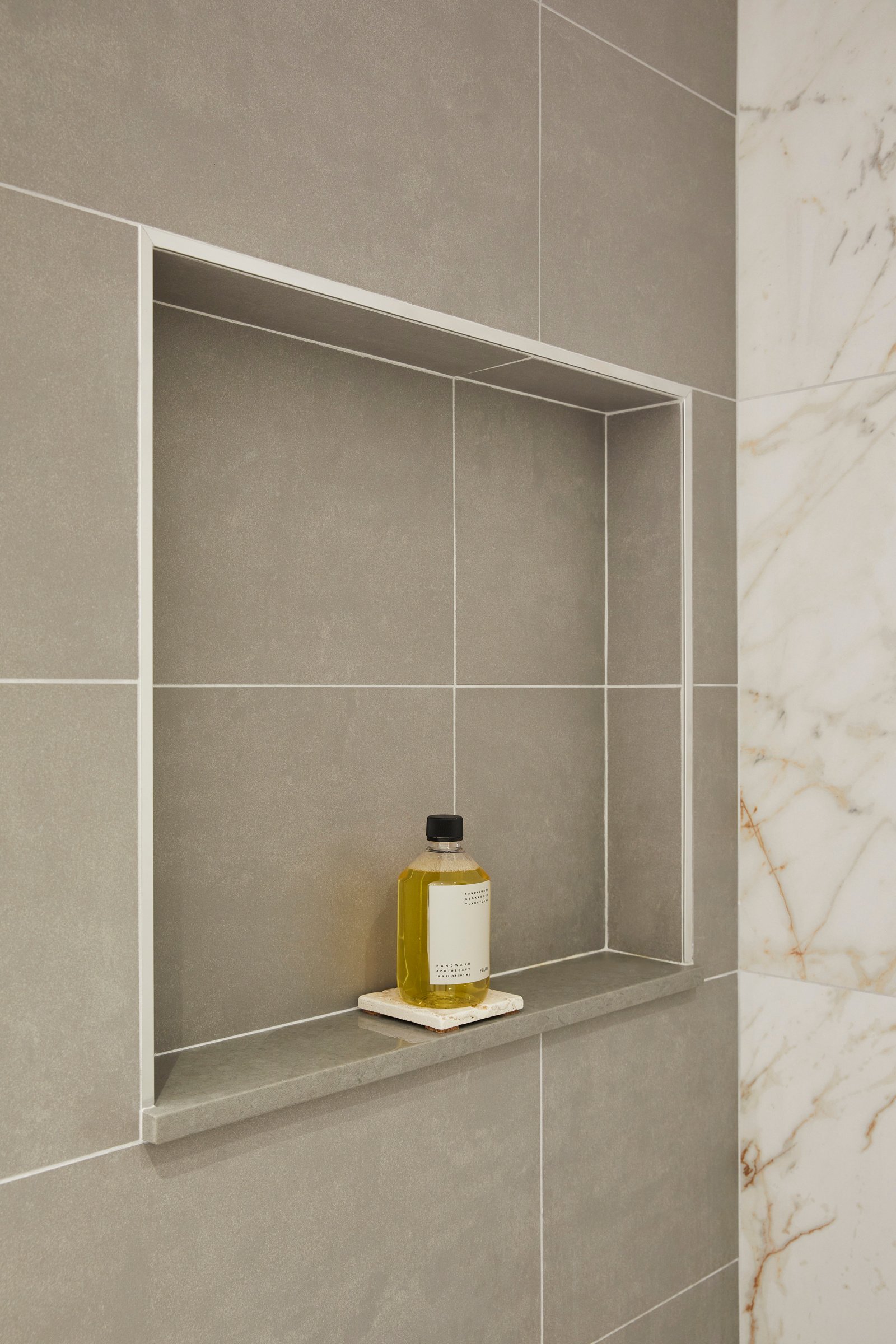 Grey tiled shower niche with a bottle of soap.