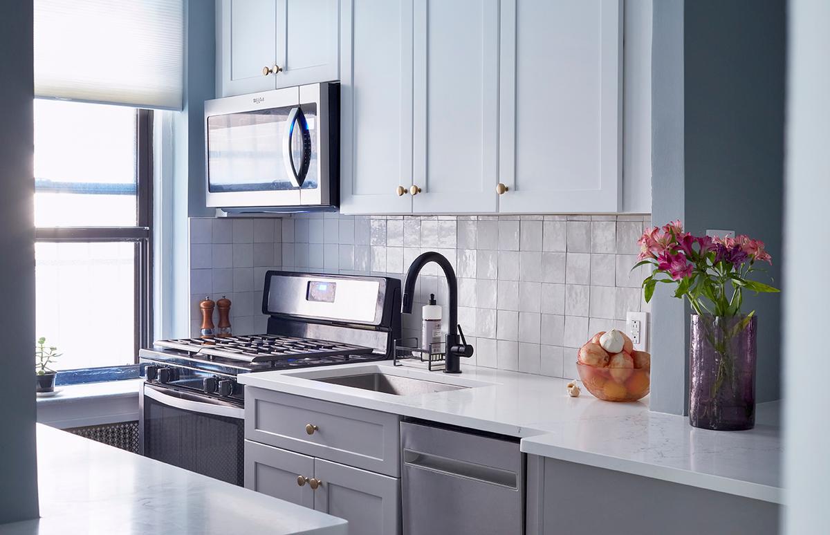 Light blue kitchen with white tiles and a black faucet.