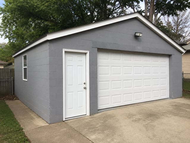 Gray painted cinder block garage with white doors.