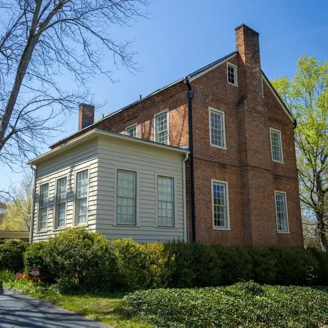 Historic brick colonial house with a wooden siding addition and hedges