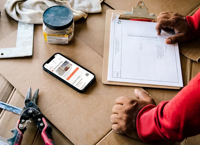 A person views blueprints, tools, and a phone on cardboard.