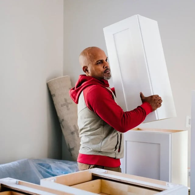 Man installing white kitchen cabinet during home renovation.