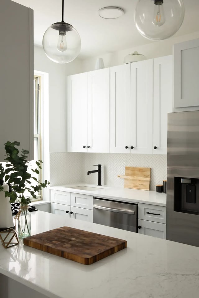 Bright white kitchen with a black faucet and globe lights.