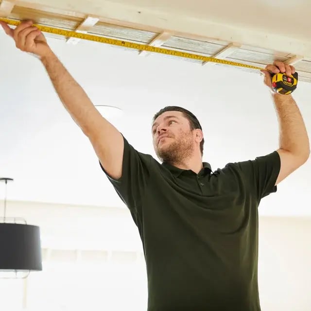A contractor measuring the ceiling with a tape measure.