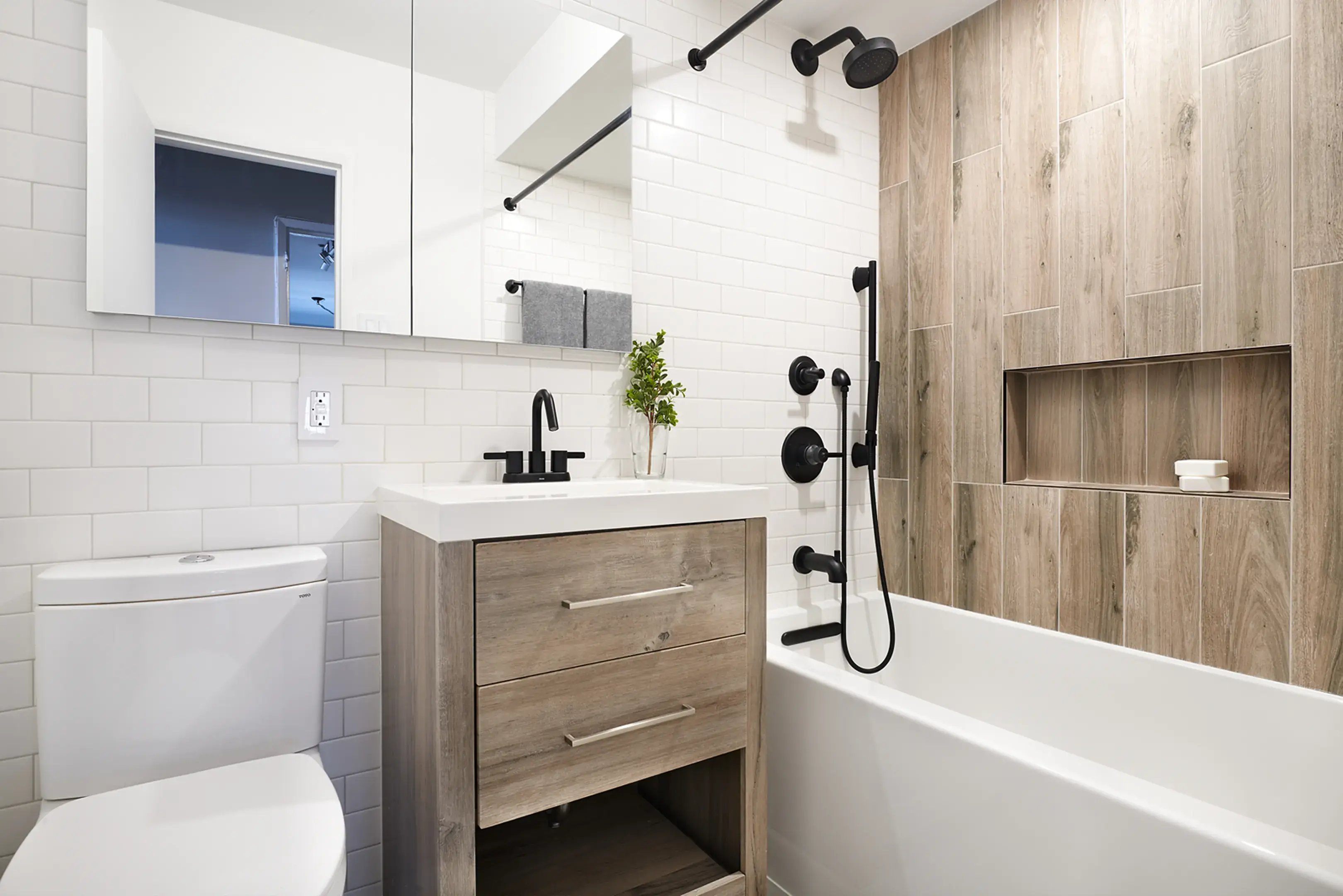 A modern bathroom featuring a wood-accented tub and black hardware.