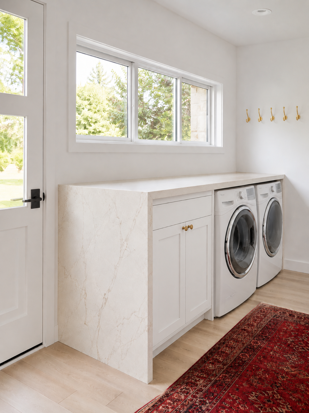Mudroom and laundry room ideas including a waterfall stone counter over side-by-side machines and a brass hook rail.