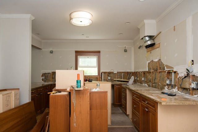 Kitchen under renovation, walls exposed, cabinets still in place.