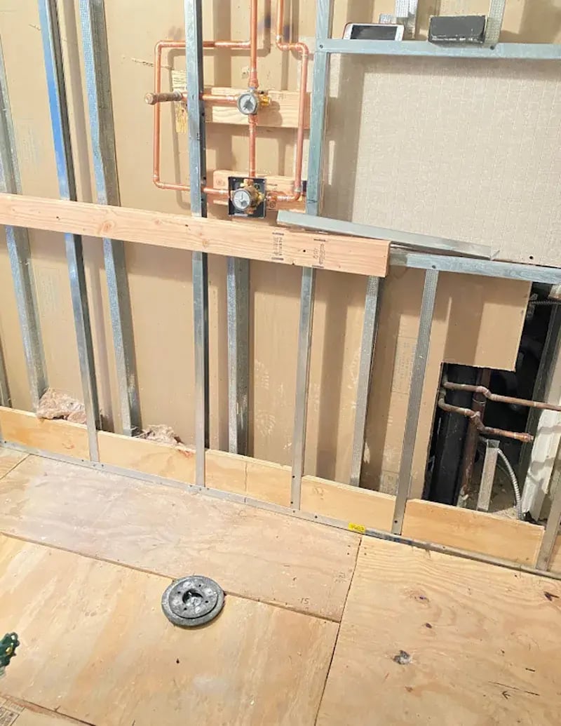 Unfinished bathroom wall framing with copper pipes.