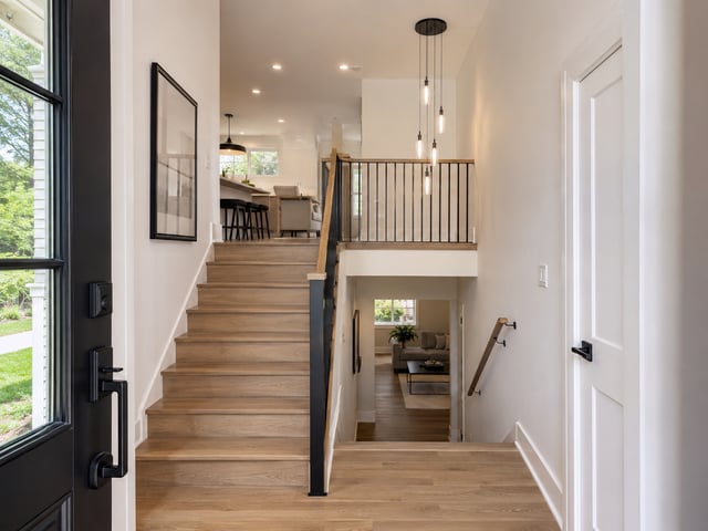 A split-level home foyer featuring light wood flooring, a staircase leading up to a kitchen area, and stairs descending toward a living room.