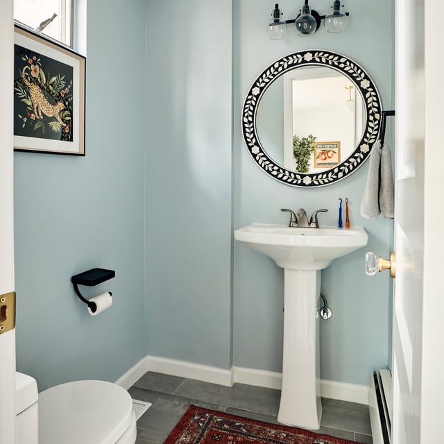 Blue half bathroom with pedestal sink and round mirror.