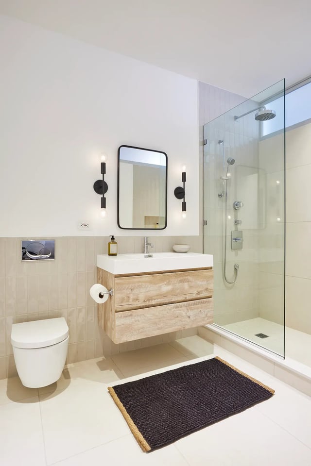 A modern bathroom featuring a floating wood vanity, a glass-enclosed walk-in shower, and a wall-mounted toilet.