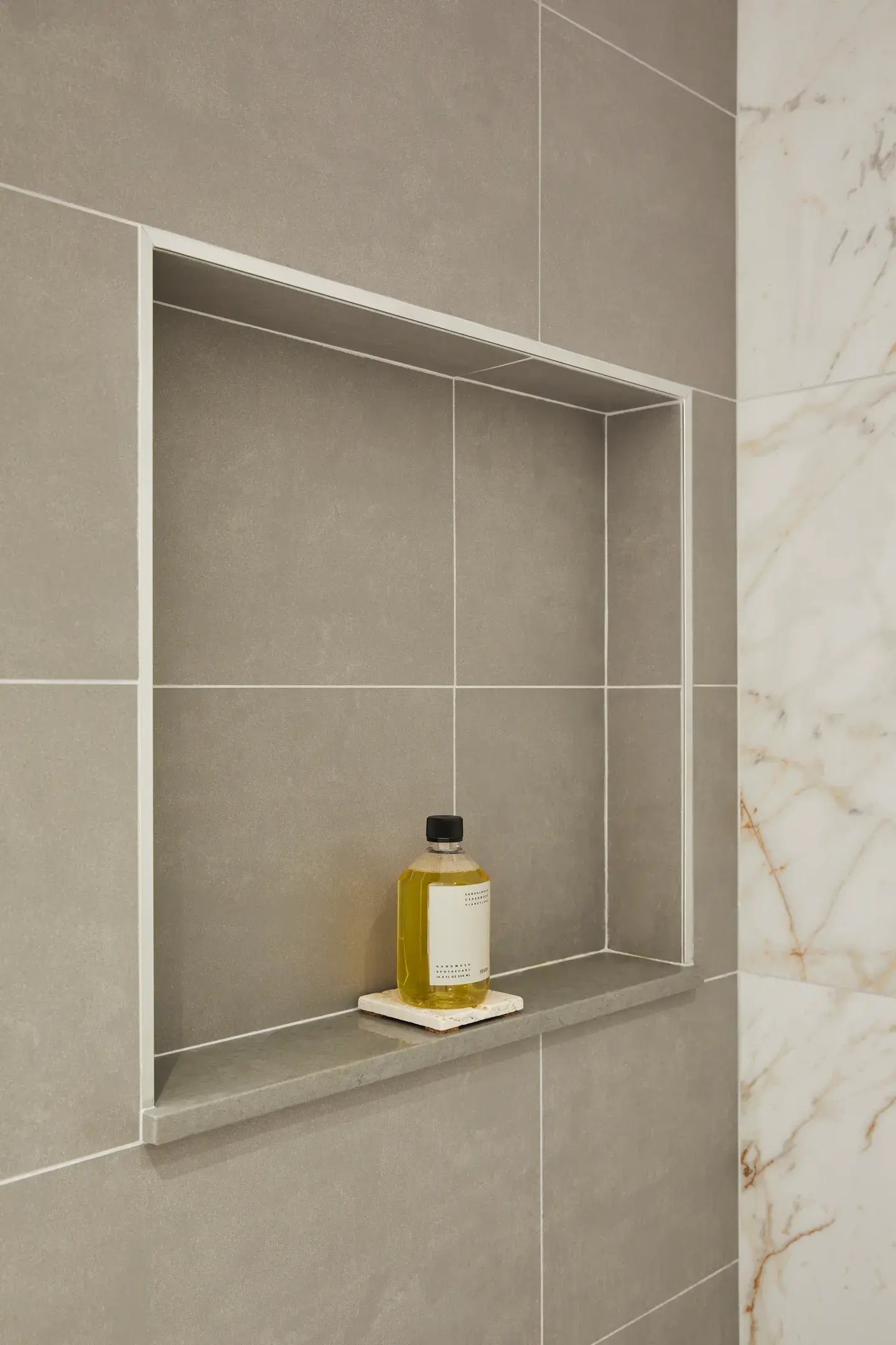 Minimalist shower with matte gray tiles and a single amber soap bottle.