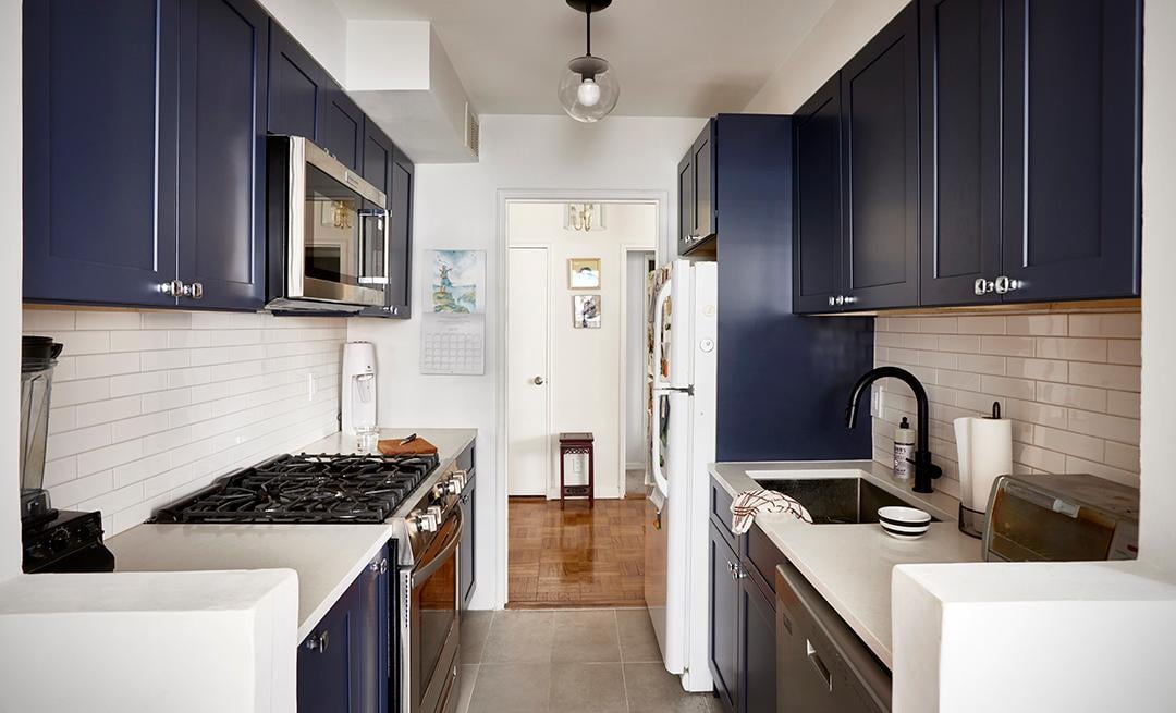 A modern kitchen featuring navy blue cabinetry, white subway tile backsplash, and stainless steel appliances.
