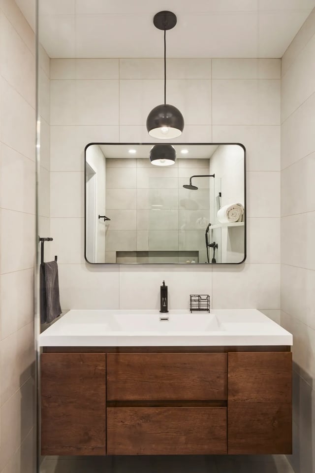 Modern bathroom vanity with wood drawers and black pendant.