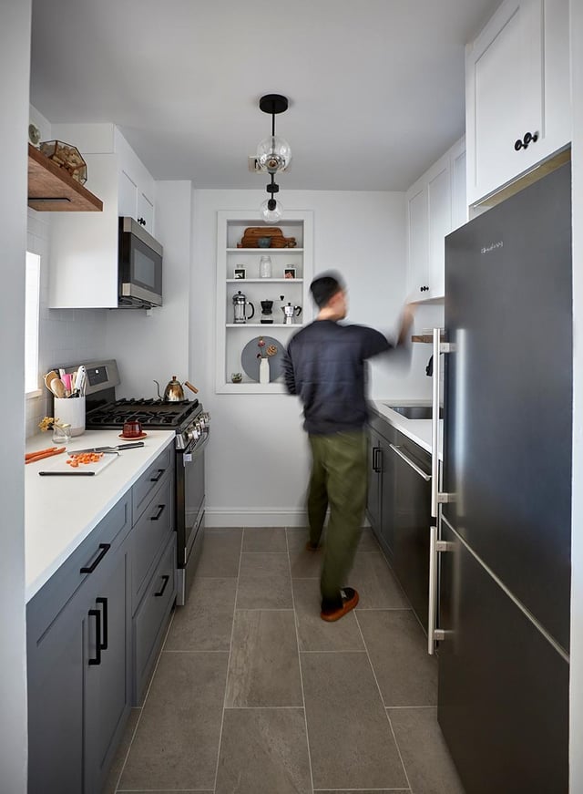 A modern, narrow galley kitchen featuring gray lower cabinetry, white upper cabinets, and a built-in recessed shelving unit filled with coffee-making accessories.