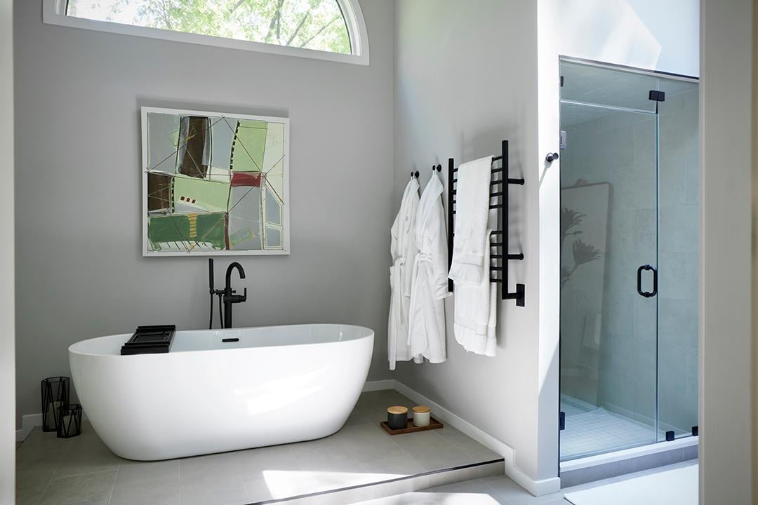 A modern bathroom featuring a white freestanding soaking tub, a glass-enclosed shower, and light gray walls.