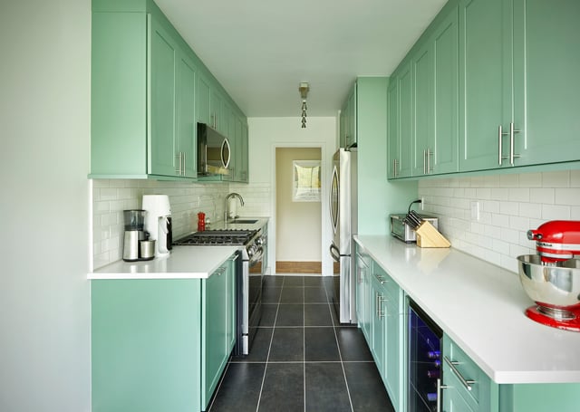 Green galley kitchen with white countertops and dark floor.
