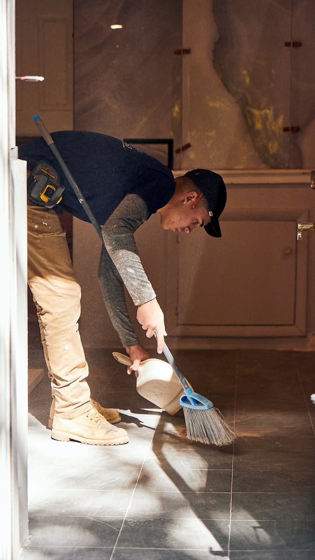 Contractor cleaning up dust with a broom and dustpan after finishing a bathroom remodel