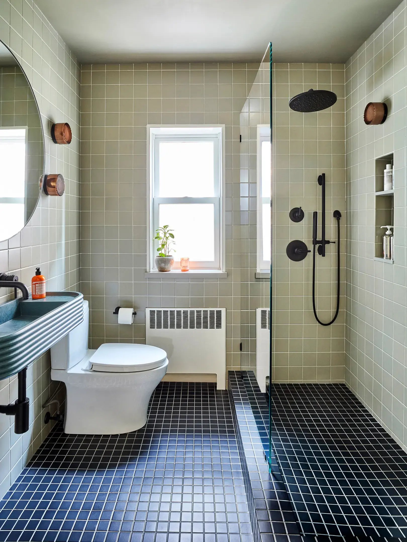 Sage green tiled bathroom with black floor and glass wall.