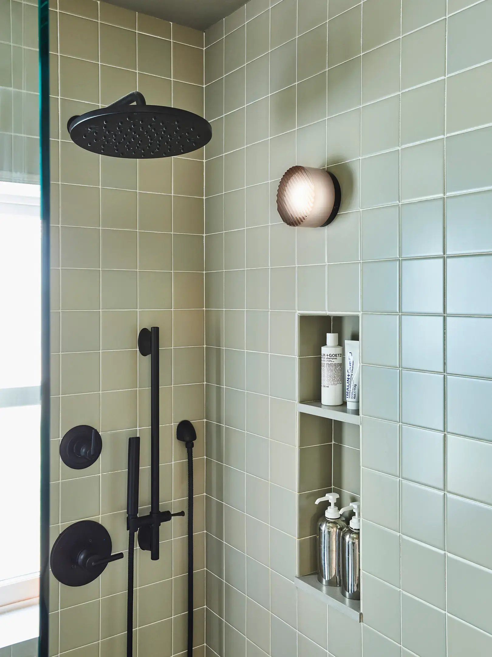 Shower with green tiles, black fixtures, and wall light.