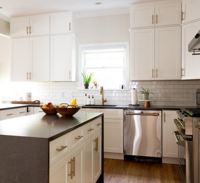 A modern kitchen featuring white shaker cabinets, gold hardware, a black countertop on the island, and stainless steel appliances.