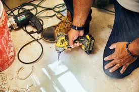 Person using a yellow power drill on a light floor surface.