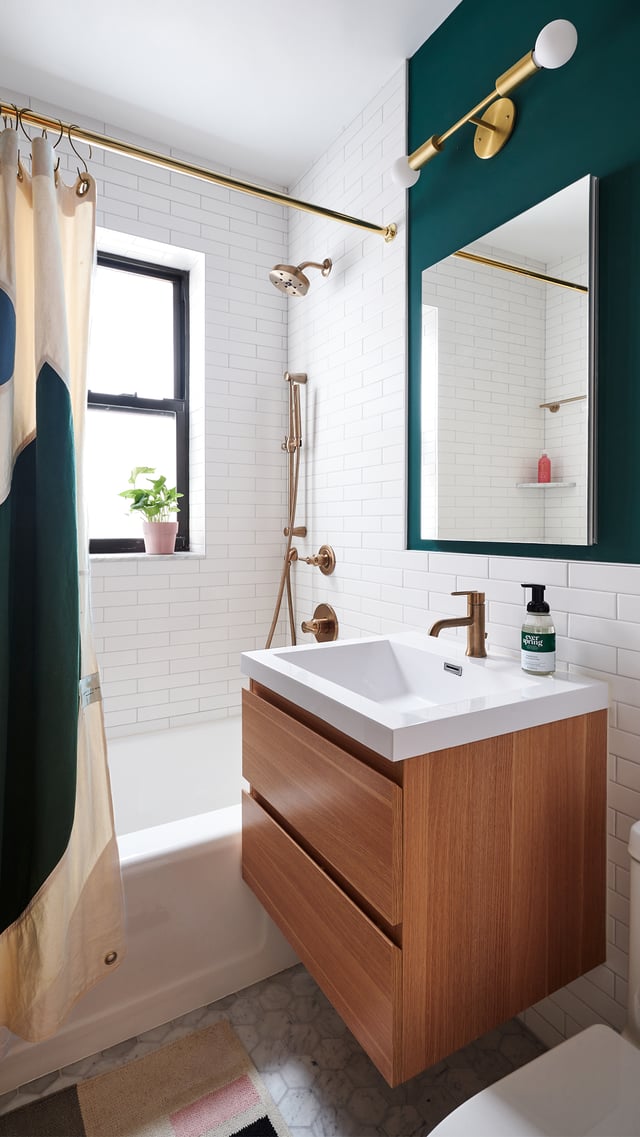 New York bathroom with green walls, white subway tile, brass fixtures, and a wood vanity