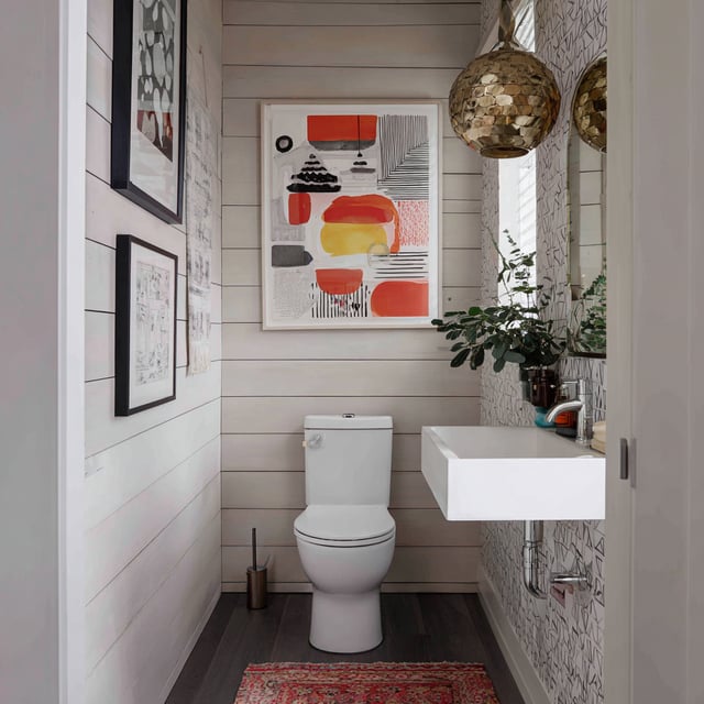 A compact washroom with shiplap walls, art, and a floating sink.