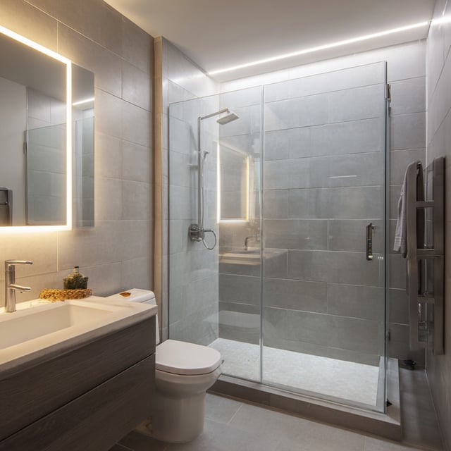 Grey bathroom with glass shower, lighted mirror and vanity.