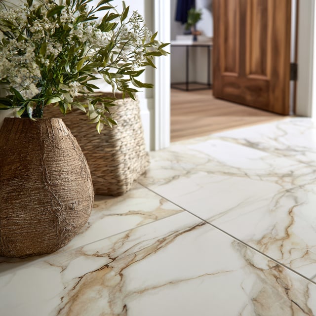 A close-up of marble-look porcelain tile with warm veining, complemented by woven textures and greenery.